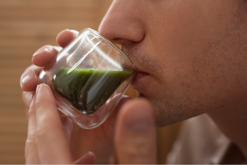 Person trinkt frisch zubereiteten Matcha Tee aus einem Glas – gesunde Matcha Zubereitung mit intensiv grüner Farbe