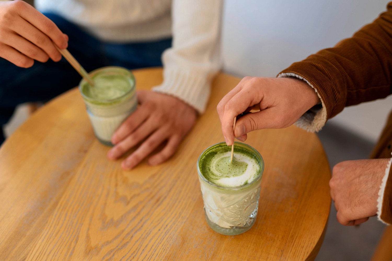 Zwei Gläser Matcha Latte werden am Tisch umgerührt – cremige Matcha Zubereitung