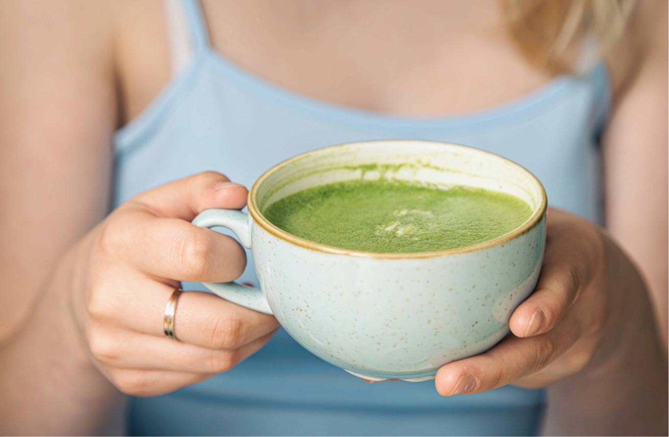 Frau hält eine Tasse Matcha Tee in der Hand – cremiger Bio Matcha