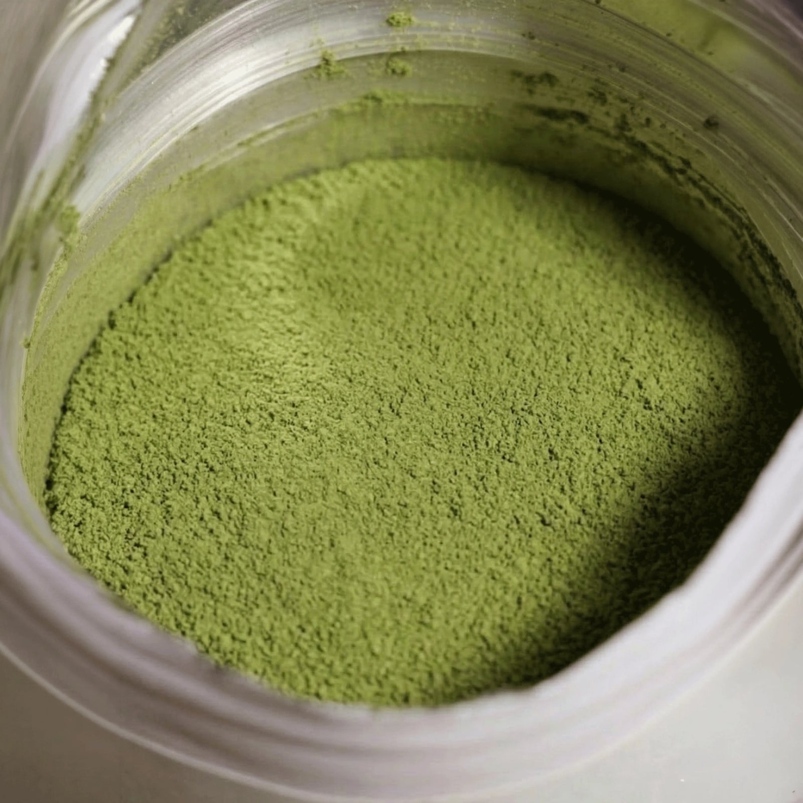 Detaillierte Nahaufnahme von feingemahlenem Raw Elements Bio 100% Matcha Pulver Ceremonial Grade in der geöffneten Verpackung.