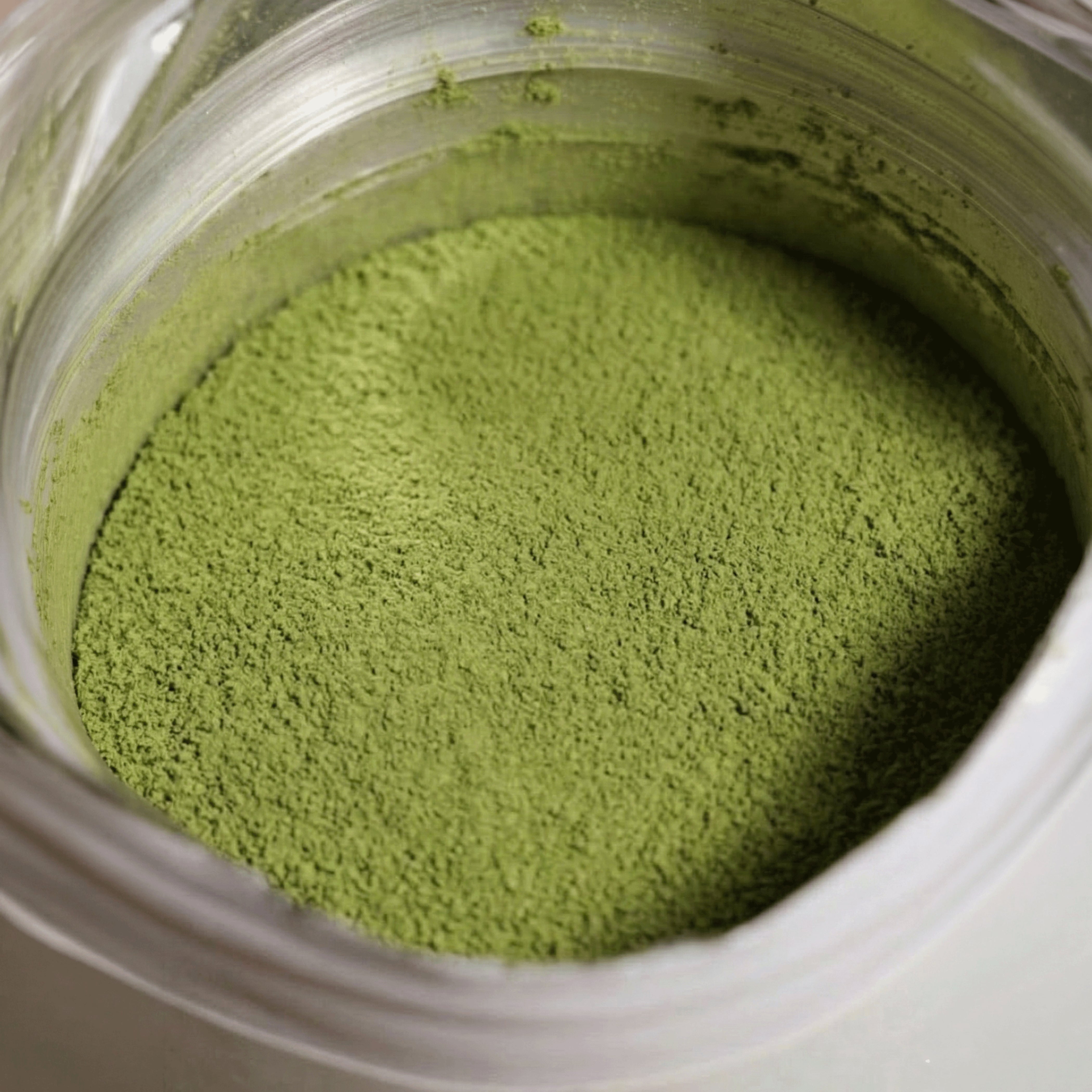 Detaillierte Nahaufnahme von feingemahlenem, leuchtend grünem Raw Elements Bio Matcha Erdbeere Pulver direkt im geöffneten Standbodenbeutel.