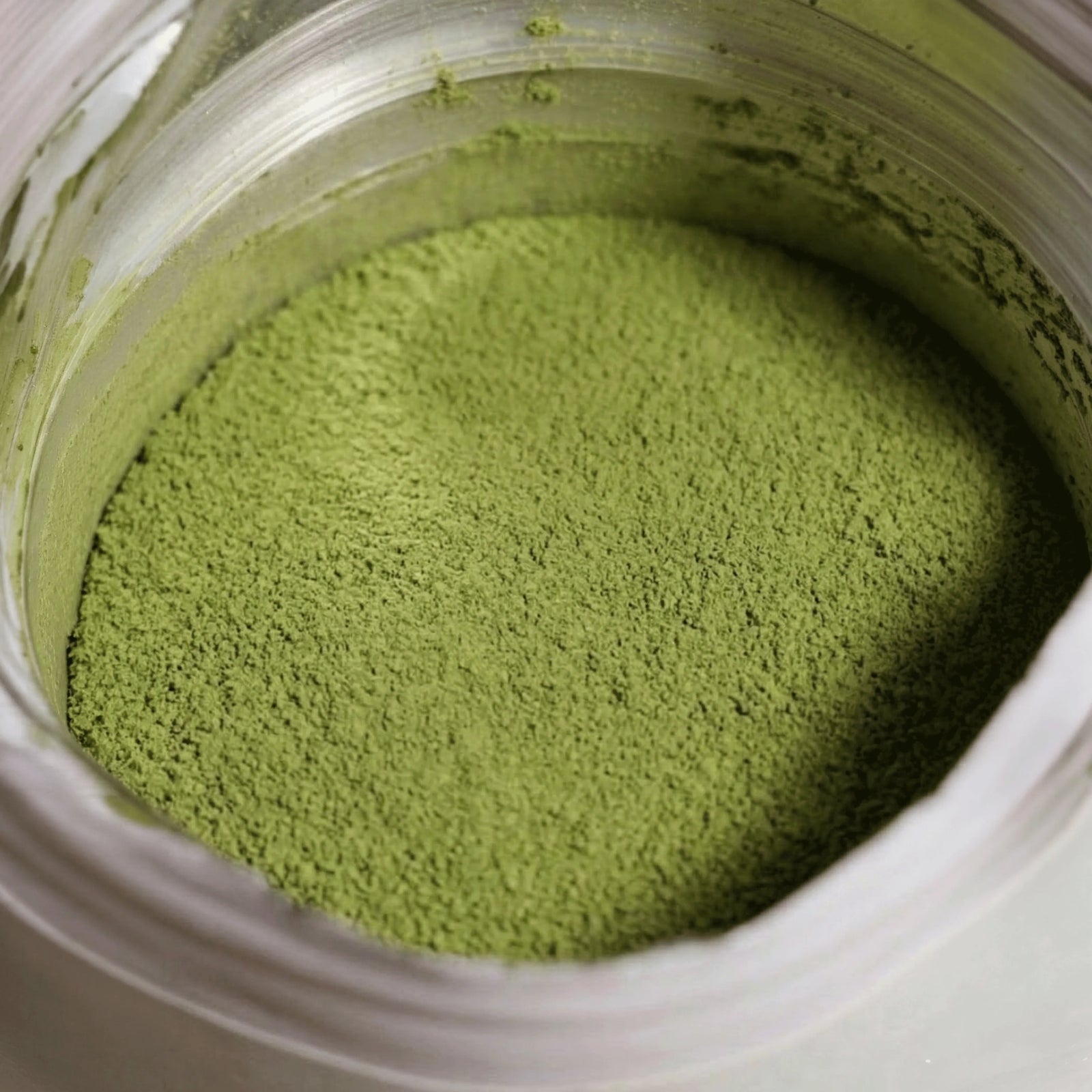 Detaillierte Makroaufnahme von leuchtend grünem Premium Bio Matcha Vanille Pulver direkt im Standbodenbeutel.
