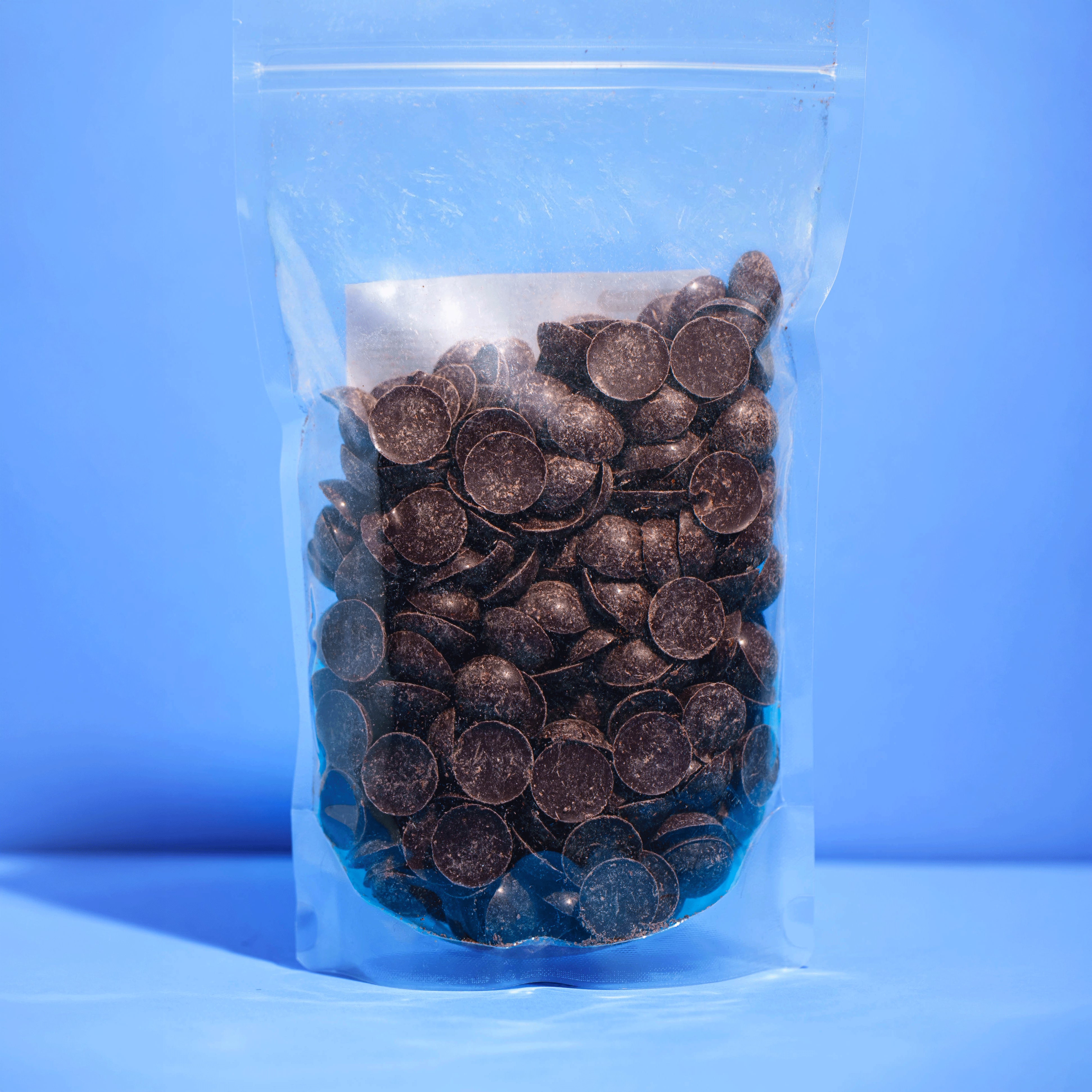 Transparenter Standbodenbeutel gefüllt mit zartschmelzenden Raw Elements Bio Schokodrops auf blauem Hintergrund.