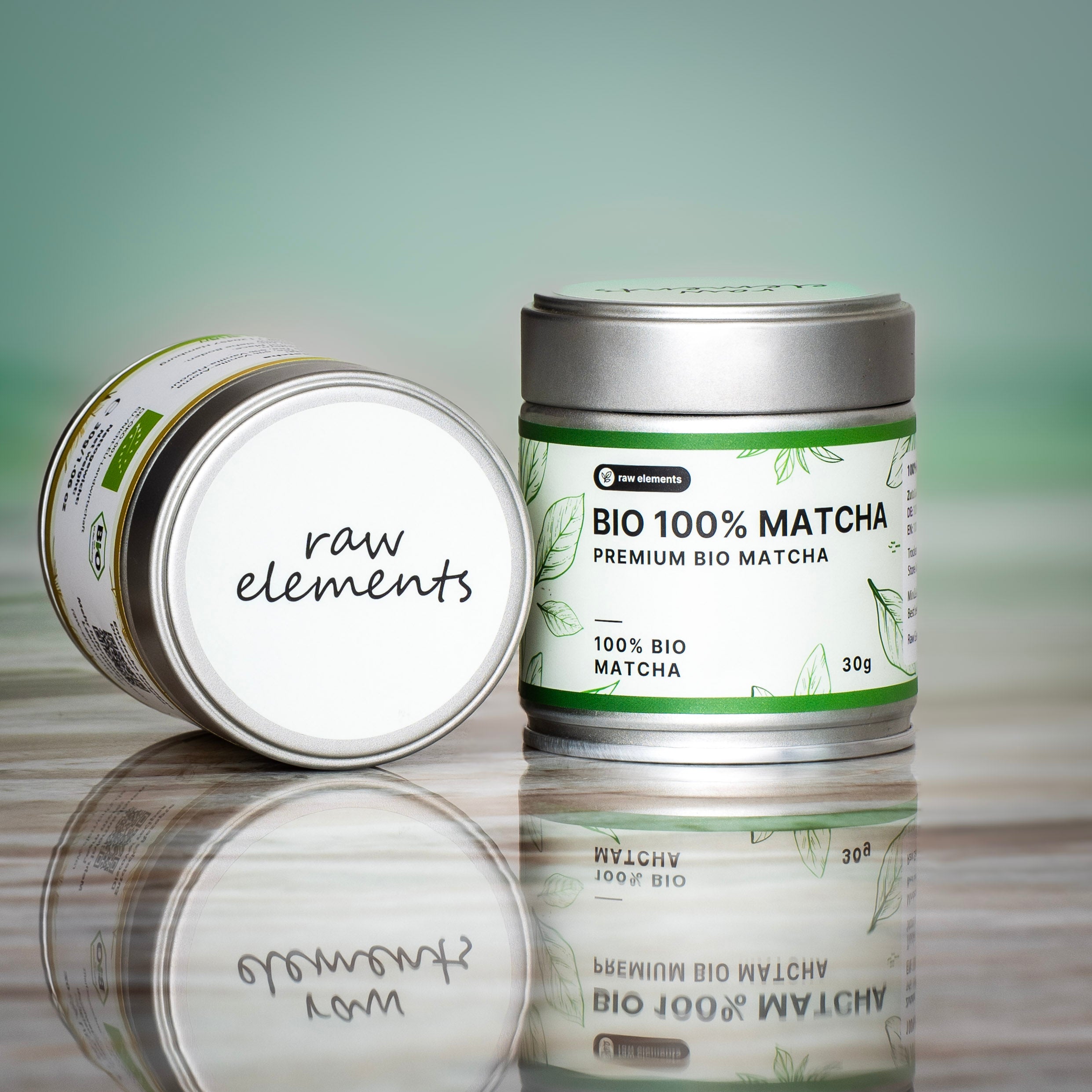 Zwei Dosen Bio Matcha Tee der Marke Raw Elements auf spiegelnder Oberfläche – hochwertiges Matcha Pulver für gesunde Zubereitung