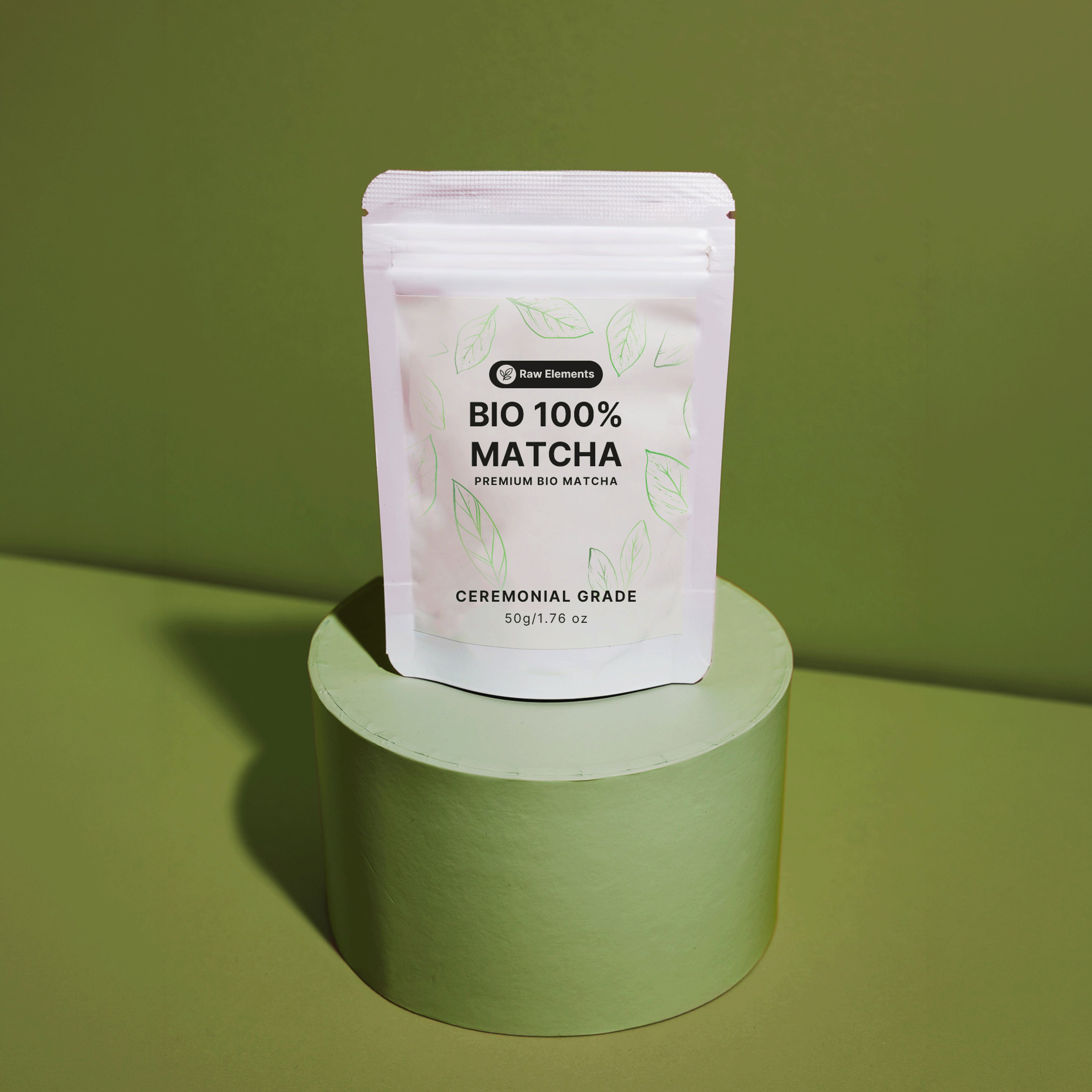 Weißer Standbodenbeutel des Raw Elements Bio 100% Matcha Ceremonial Grade, platziert auf einem runden, olivgrünen Podest.