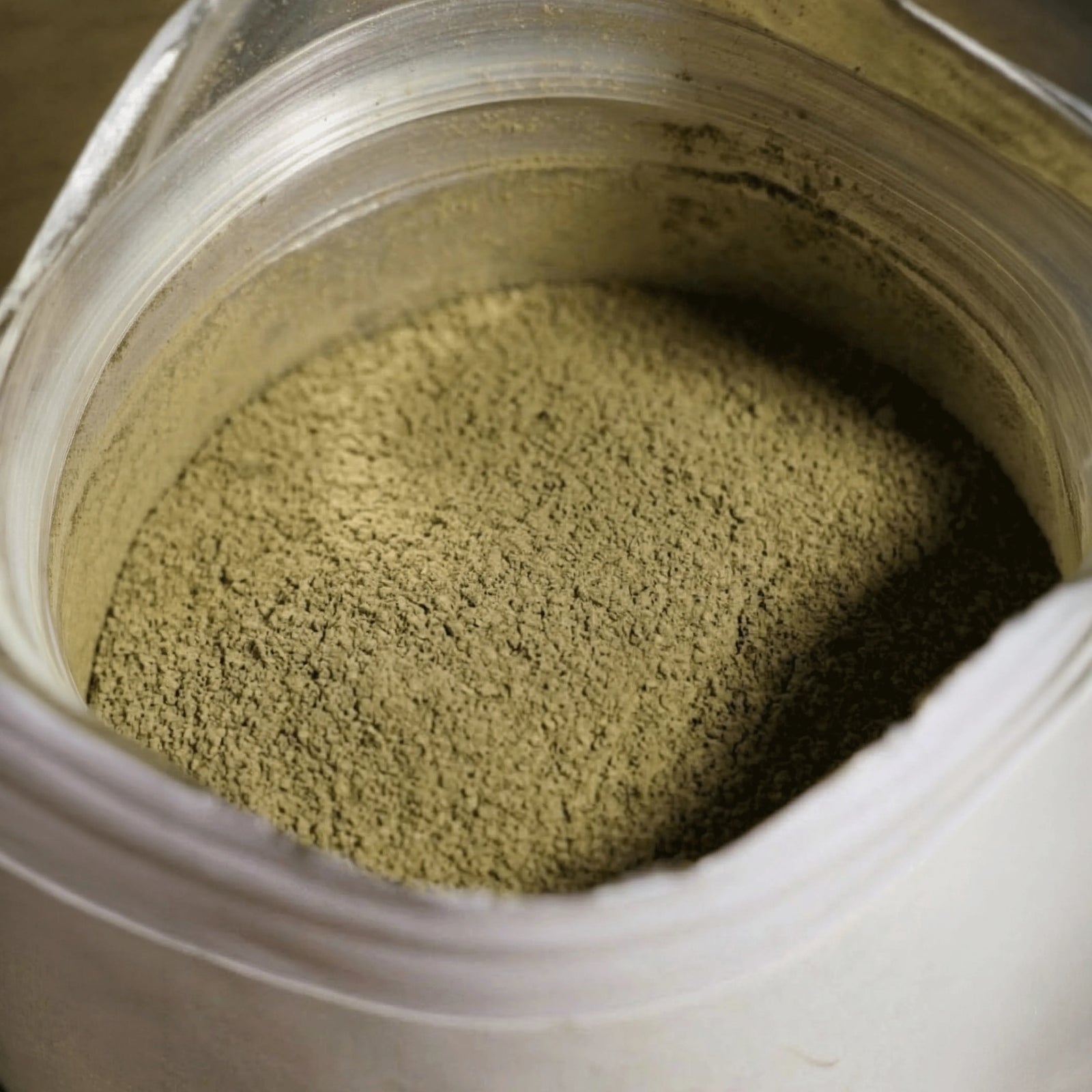 Detaillierte Nahaufnahme von feingemahlenem, geröstetem Raw Elements Bio-Hojicha Pulver im Inneren der geöffneten Verpackung.