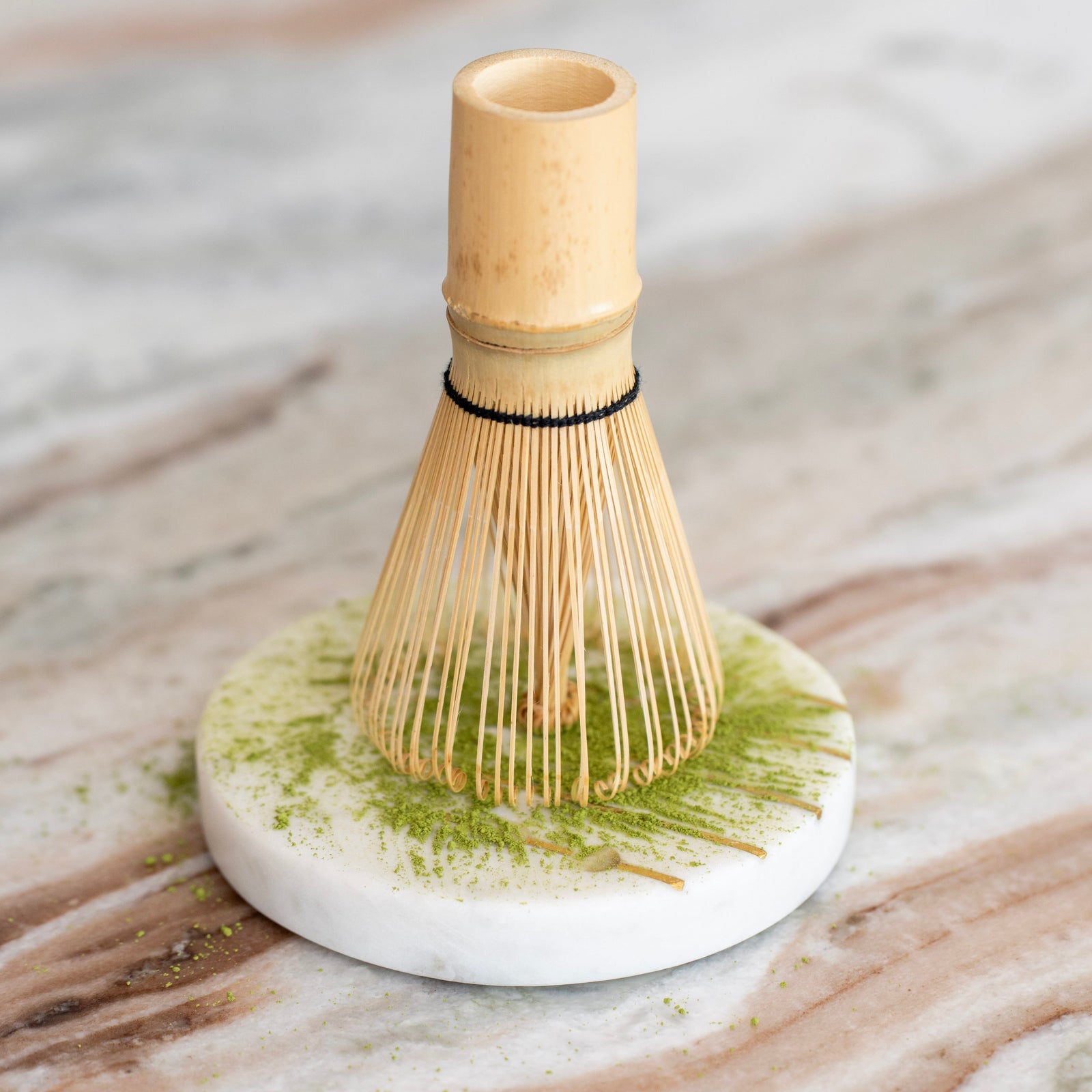 Chasen Matchabesen aus Bambus auf einem Marmor-Untersetzer mit fein gemahlenem Matcha-Pulver