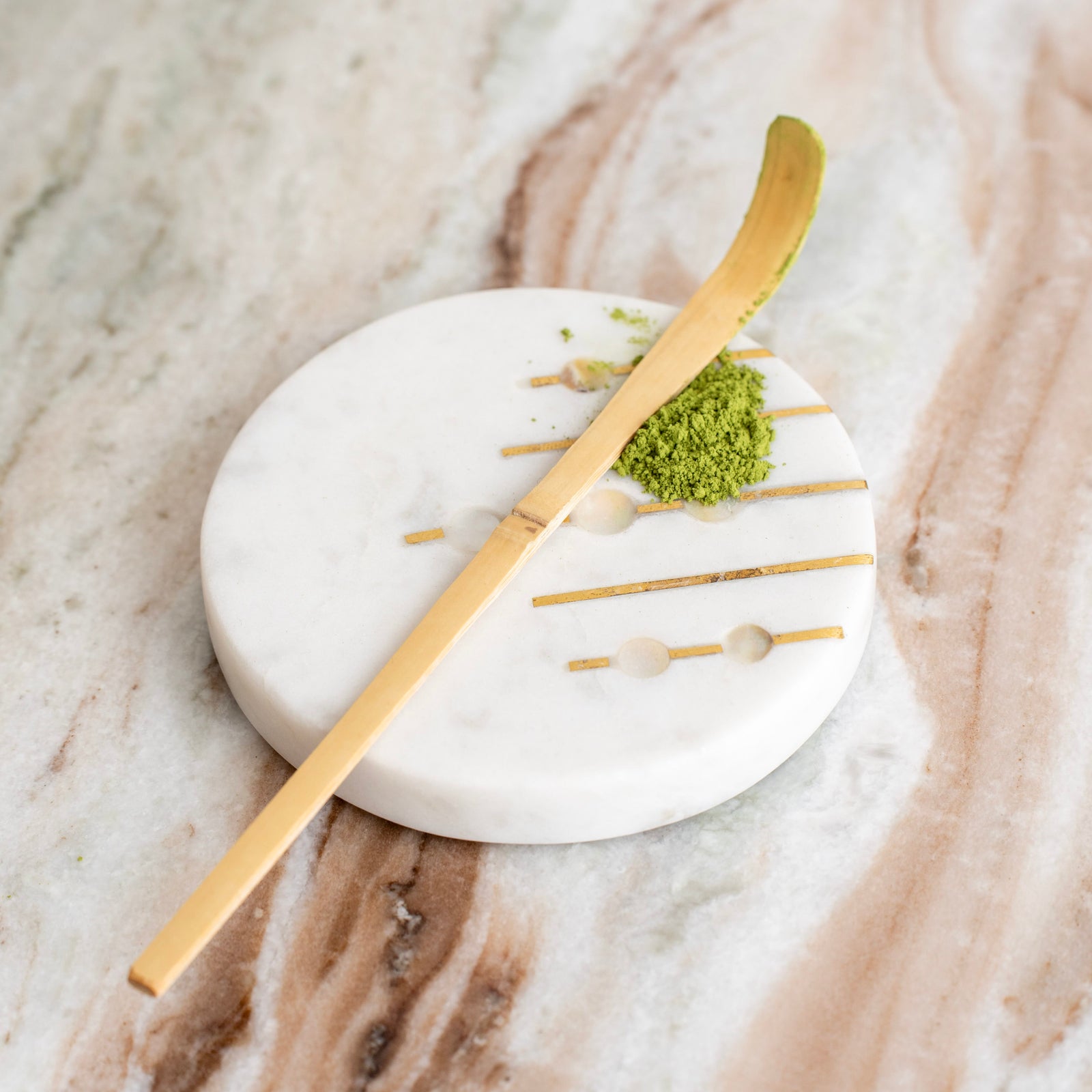 Nahaufnahme eines Chashaku Matcha-Löffels aus Goldbambus mit einem Häufchen Matcha-Pulver auf Marmor