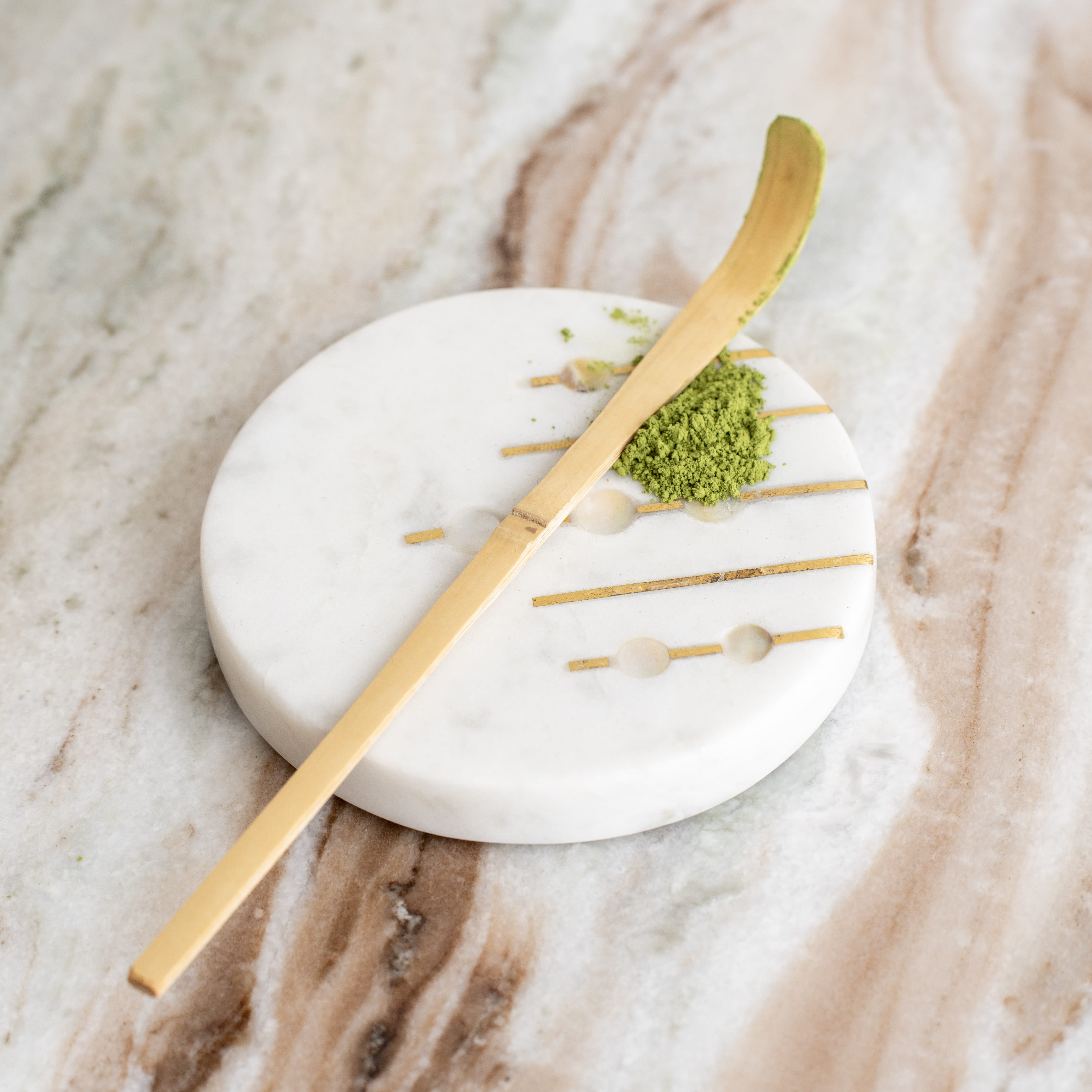 Nahaufnahme eines Chashaku Matcha-Löffels aus Goldbambus mit einem Häufchen Matcha-Pulver auf Marmor