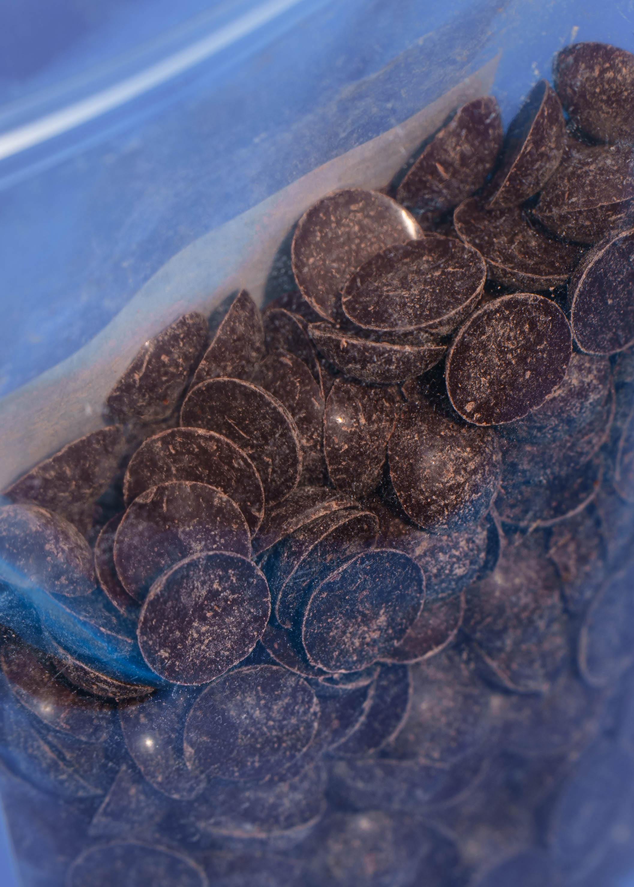 Detailaufnahme der Textur von dunklen, runden Bio-Schokoladendrops in einem transparenten Beutel. Die Schokodrops sind vegan und nur mit Dattelsüße gesüßt.
