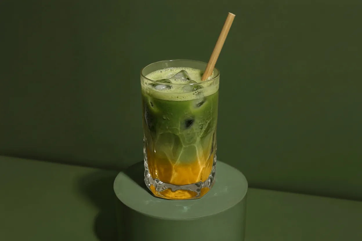 Ein frisch zubereiteter, eiskalter Iced Mango Matcha Latte im Glas mit Eiswürfeln und einem Bambus-Trinkhalm